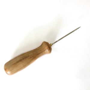 May include: A wooden-handled awl with a metal needle. The awl is used for piercing holes in leather or other materials.