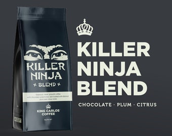 May include: A black bag of King Carlos Killer Ninja Blend coffee with a white crown logo and a graphic of a ninja's eyes. The text on the bag reads "Killer Ninja Blend" and "Chocolate Plum Citrus".