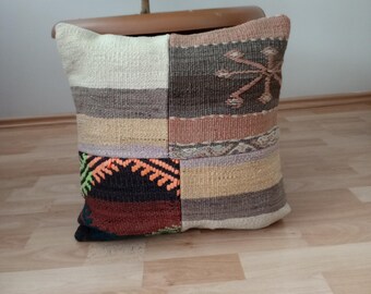 May include: A square patchwork pillow with a variety of colors and patterns, including brown, beige, white, and orange. The pillow is made of woven fabric and has a fringed edge.