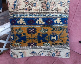 May include: Square decorative pillow with a vintage rug design. The pillow features a cream-colored top and bottom with floral patterns, a blue and gold center section with geometric shapes, and a blue stripe.