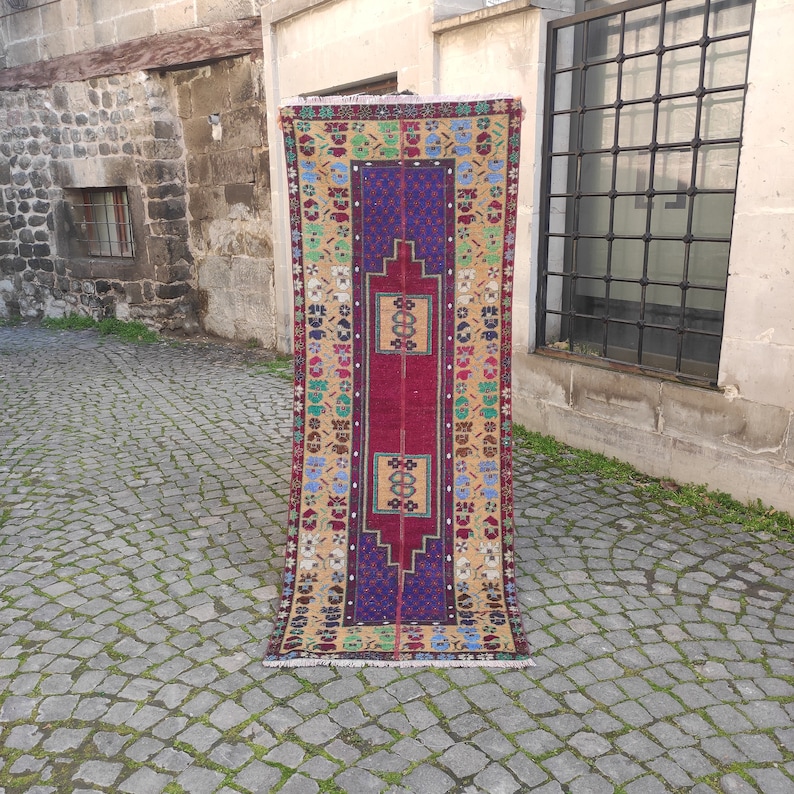 May include: A long, narrow rug with a red center and a colorful border. The rug has a traditional Turkish design with geometric patterns and floral motifs. The rug is made of wool and is in good condition.