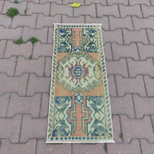 May include: A rectangular, hand-woven rug with a central medallion design. The rug features a palette of orange, green, blue, and cream colors. Geometric patterns and floral motifs adorn the rug's surface, with a fringed edge along the bottom.