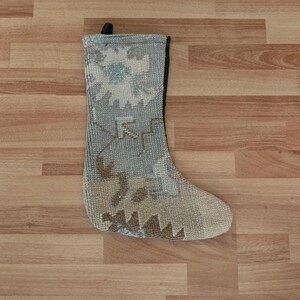 May include: A gray and beige patterned stocking with a black cuff. The stocking is made of a woven fabric and has a traditional design.