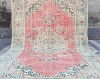 Peut inclure: Un grand tapis rectangulaire présentant un champ central rose corail délavé avec un motif de médaillon complexe en bleu sarcelle doux et crème. La bordure affiche des motifs floraux répétitifs dans des tons sourds de bleu, vert et crème.