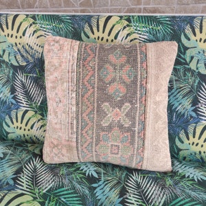 Op de afbeelding: Een decoratief kussen met een vintage, handgeweven ontwerp in beige, roze en groene tinten. Het kussen is gemaakt van een zachte, textuurrijke stof en heeft een traditioneel geometrisch patroon.