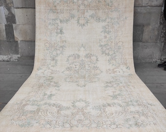 May include: A large, off-white rug with a delicate floral pattern in shades of green and brown. The rug has a distressed, vintage look and is folded in half.