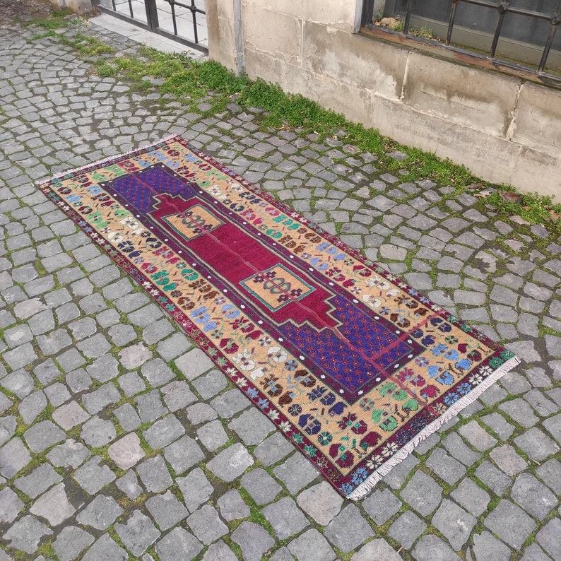 May include: A long, rectangular rug with a colorful, intricate pattern. The rug has a red center with a blue and white border. The rug is laid out on a cobblestone path.