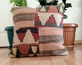May include: A colorful, patterned throw pillow with a geometric design in shades of brown, red, beige, and gray. The pillow is made of woven fabric and has a soft, textured surface.