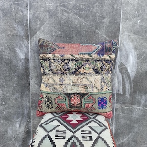 May include: A rectangular patchwork pillow with a variety of patterned fabric sections in shades of red, blue, green, and beige. The pillow is placed on a patterned cushion with a geometric design.