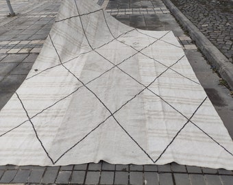 May include: A white rug with a black diamond pattern. The rug is folded in half and lying on a gray concrete surface.