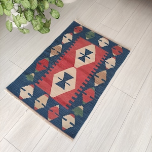May include: A blue, red and beige patterned rug with a fringed edge. The rug has a geometric design with diamond shapes and a central motif of two stylised butterflies.