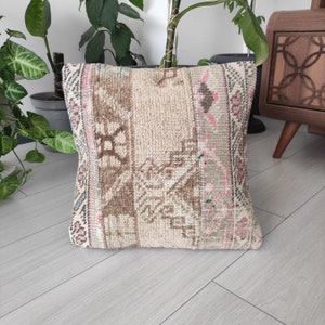 Op de afbeelding: Een beige en roze gepatroneerd kussen met een geweven textuur. Het kussen is gemaakt van een vintage tapijt en heeft een vervaagde uitstraling.