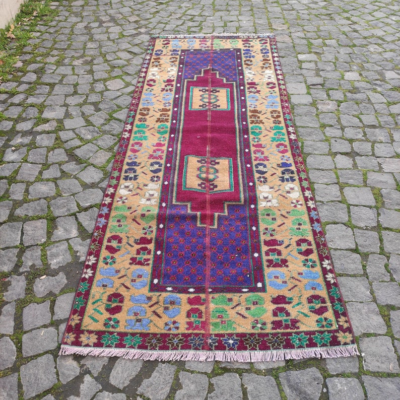May include: A long, narrow rug with a red, purple, and beige pattern. The rug has a fringe on both ends.