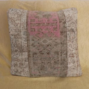 Op de afbeelding: Vierkant decoratief kussen met een centraal roze bloemmotief op een bruine achtergrond. Het kussen heeft een getextureerde, geweven uitstraling met patroonranden in beige en bruin. Het ligt op een lichtgele ondergrond. Afmetingen: circa 40 cm x 40 cm.
