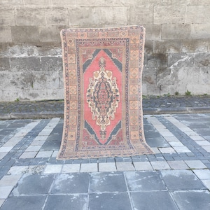 May include: A vintage Turkish rug with a traditional geometric pattern in shades of red, pink, blue, and beige. The rug has a faded, worn look, giving it a unique character.