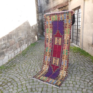 May include: A colorful vintage Turkish rug with a red, blue, and yellow geometric pattern. The rug is hand-woven and has a fringed edge.