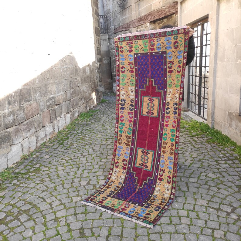 May include: A colorful vintage Turkish rug with a red, blue, and yellow geometric pattern. The rug is hand-woven and has a fringed edge.