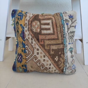 May include: A square throw pillow with a patchwork design. The pillow is made of different fabrics with various patterns in shades of brown, beige, blue, and yellow.