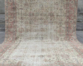 May include: A large rectangular area rug featuring a faded, distressed aesthetic with a complex floral and geometric pattern. The color palette consists of muted shades of dusty rose, sage green, and cream, framed by a wide, ornate decorative border.