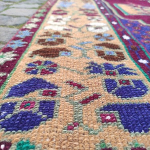May include: Close-up of a colorful rug with a floral pattern. The rug has a beige background with blue, red, and green accents. The rug is woven with a variety of textures.