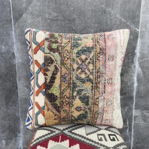 Op de afbeelding: Vierkant decoratief kussen met een patchwork ontwerp. Het kussen heeft een mix van kleuren, waaronder beige, bruin, groen en roze. Het kussen heeft een vintage, distressed look, met een patroon.