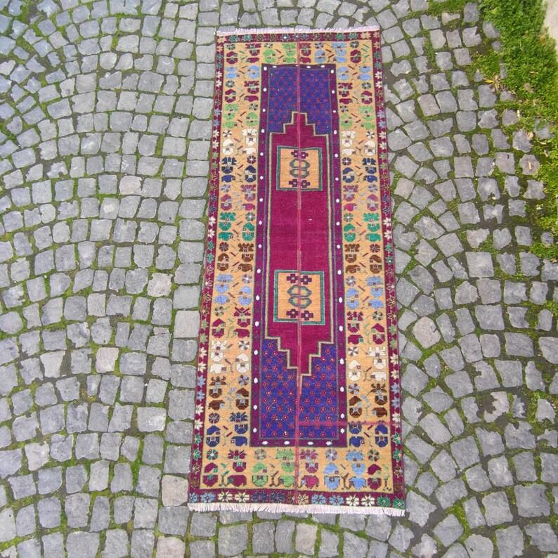 May include: A long, narrow rug with a traditional Turkish design. The rug has a red center with a blue and purple border. The border is decorated with a floral pattern in shades of yellow, green, and blue.