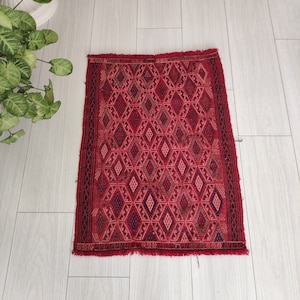 May include: A red and black patterned rug with a diamond design. The rug has a fringed edge.