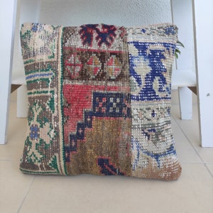 May include: A patchwork pillow with a variety of colors and patterns, including red, blue, green, and brown. The pillow is made of woven fabric and has a fringed edge.