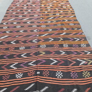 May include: A black and orange patterned rug with geometric designs. The rug has a traditional Moroccan style.