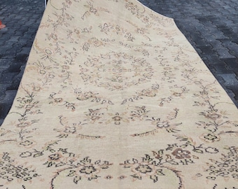 May include: A beige rug with a floral pattern in shades of brown and cream. The rug has a fringed edge and is made of a soft, woven material.