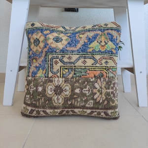 May include: A decorative pillow with a patchwork design featuring blue, green, orange, and brown colors. The pillow is made from a woven fabric with intricate patterns.