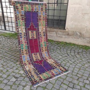 May include: A vintage Turkish rug with a colorful geometric pattern in shades of red, blue, yellow, and green. The rug has a fringe border and is made of wool.