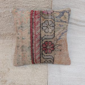 May include: Square decorative pillow with a patchwork design. The pillow features a mix of colors including beige, red, and blue. The design includes floral and geometric patterns, creating a vintage aesthetic.