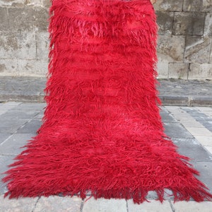 May include: A bright red shaggy rug with long fringe. The rug is made of wool and has a soft, fluffy texture.