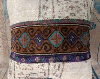 May include: A white throw pillow with a brown, purple, and turquoise patterned border. The pillow is made from a woven fabric and has a slightly distressed look.