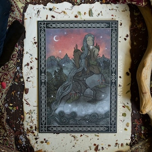 Può includere: Una stampa artistica con un'illustrazione mistica di una figura con lunghi capelli fluenti, seduta su una roccia con una cascata. L'opera d'arte è incorniciata con un bordo decorativo e ambientata su uno sfondo di montagne, una luna crescente e stelle.