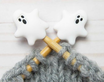 May include: Two wooden knitting needles with white ghost-shaped stitch markers. The needles are crossed and the gray yarn is wrapped around them.