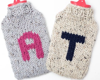 Può includere: Due bottiglie di acqua calda a maglia con un coperchio rosso. Una bottiglia è grigia con una "A" rosa e l'altra è beige con una "T" blu scuro.
