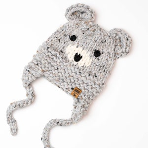 May include: Gray knitted hat with bear ears and a white face. The hat has a brown tag with the text "Little & Brave" on it.