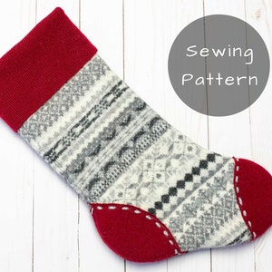 May include: A red and white knitted Christmas stocking with a gray and white patterned design. The stocking has a red cuff and a red toe. The stocking is lying on a white wooden surface. Sewing Pattern.