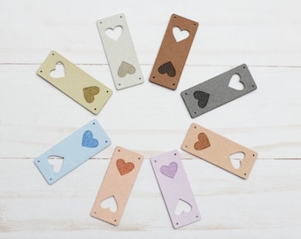 May include: Eight rectangular fabric patches with a heart-shaped cutout in the centre. The patches are in various colours, including light blue, light pink, light brown, grey, and beige. Each heart has a different colour glitter inside.