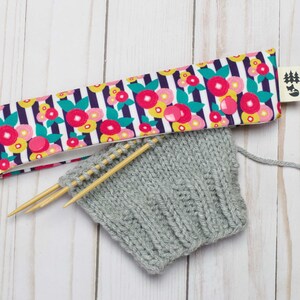 May include: A gray knitted fabric with wooden knitting needles and a floral patterned fabric needle holder. The needle holder has a small tag with a tree and fox design.