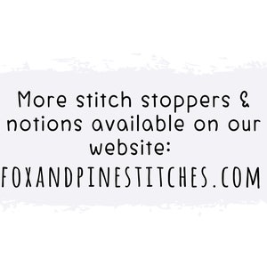 May include: A white rectangular graphic with a light purple brushstroke background featuring black text that reads: More stitch stoppers & notions available on our website: FOXANDPINESTITCHES.COM. The text is centered and uses a simple sans-serif font.