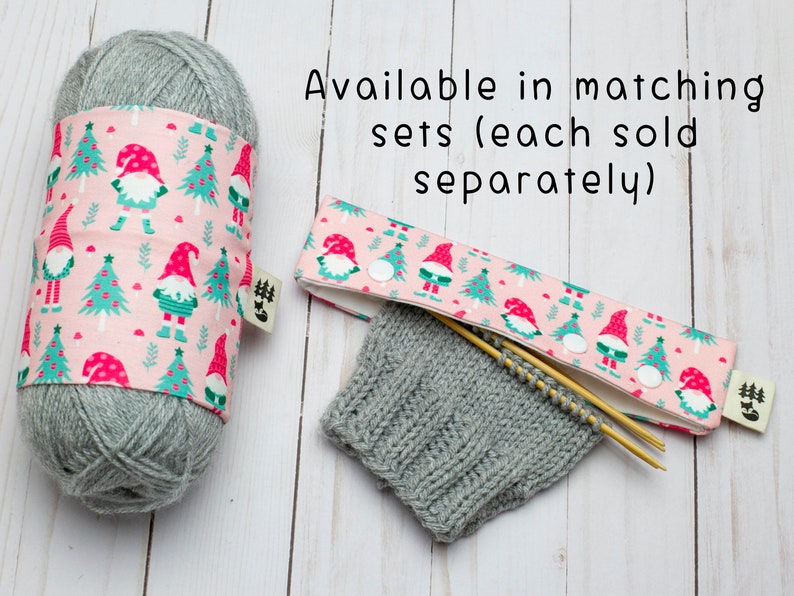 May include: A gray yarn ball wrapped with a pink fabric featuring a gnome and Christmas tree pattern. A matching knitting needle case and knitted gray swatch are also shown. Text reads: Available in matching sets (each sold separately).
