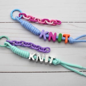 Puede incluir: Dos llaveros de paracord azul claro y verde menta, cada uno unido a una anilla de plástico y una cadena a juego. Uno tiene cuentas de colores que forman la palabra KNIT, mientras que el otro tiene cuentas metálicas plateadas con KNIT.