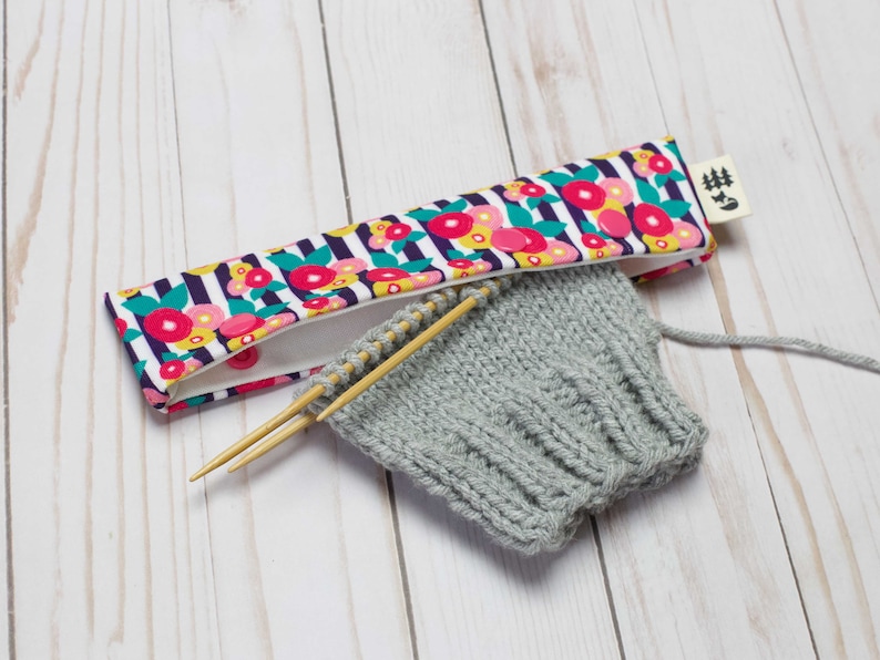 May include: A gray knitted hat with wooden knitting needles and a floral patterned fabric needle holder with the text "#5".