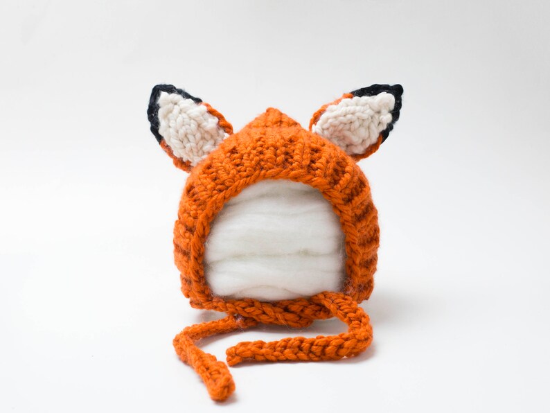 May include: An orange knitted fox hat with black and white ears and a long orange tie