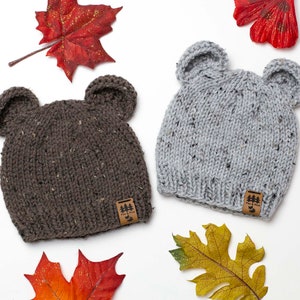 May include: Two knitted hats with bear ears. The hats are brown and grey with a brown leather tag that says "Park & Pine".
