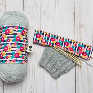 May include: A skein of light blue yarn with a floral patterned fabric cover, a knitted hat, and two wooden knitting needles.