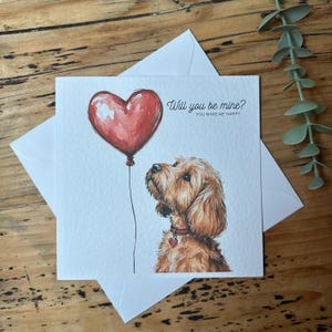 May include: A greeting card featuring a red heart balloon and a brown dog looking up at it. The card reads "Will you be mine? You make me happy."